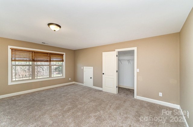 unfurnished bedroom with carpet floors, visible vents, a spacious closet, and baseboards