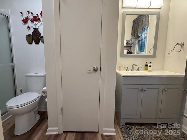 bathroom featuring toilet, a shower with shower door, wood finished floors, and vanity