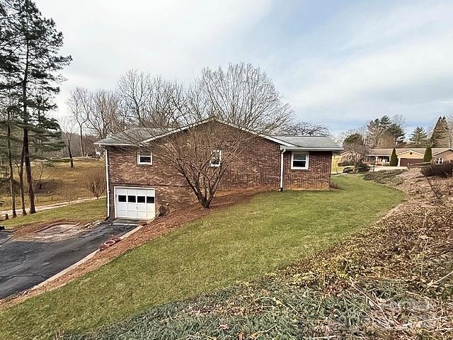 view of home's exterior featuring a garage, aphalt driveway, a lawn, and brick siding