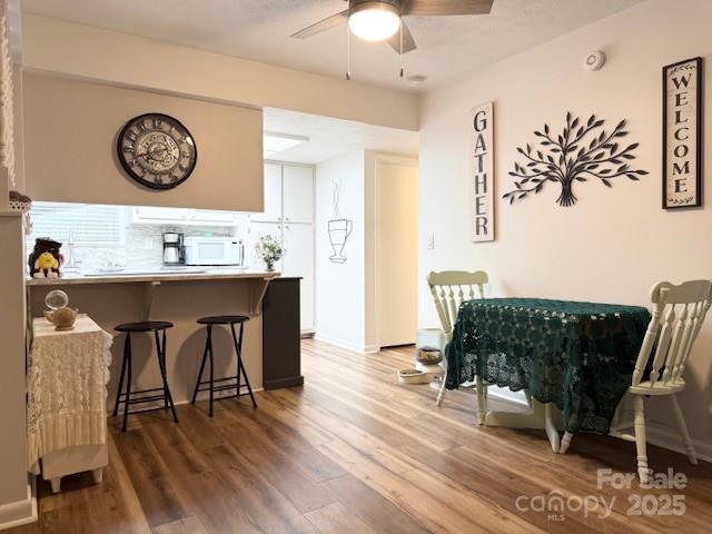 kitchen featuring a ceiling fan, white microwave, wood finished floors, a peninsula, and a kitchen bar