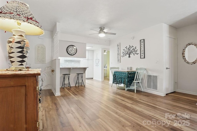 interior space with baseboards, a ceiling fan, visible vents, and light wood-type flooring