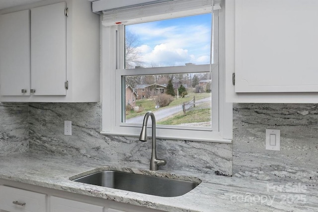 kitchen featuring a sink, decorative backsplash, light stone countertops, and white cabinetry