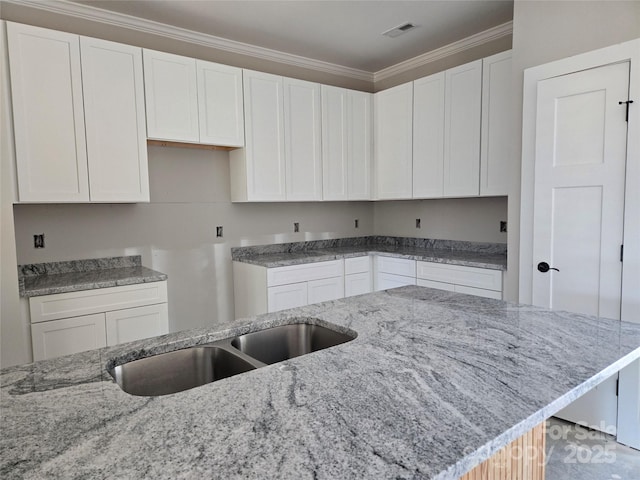 kitchen featuring light stone counters, white cabinets, visible vents, and ornamental molding