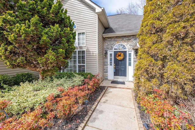 entrance to property featuring stone siding and roof with shingles