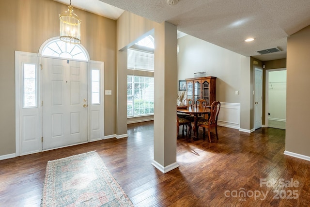 foyer entrance with a textured ceiling, visible vents, a chandelier, and dark wood-type flooring