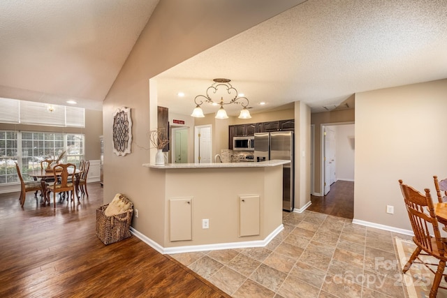 kitchen with dark brown cabinetry, light wood-style flooring, appliances with stainless steel finishes, vaulted ceiling, and light countertops