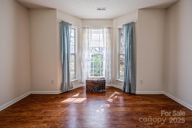 empty room with baseboards, a textured ceiling, visible vents, and wood finished floors