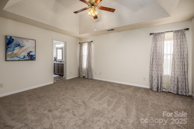 carpeted empty room featuring ceiling fan, baseboards, visible vents, and a raised ceiling