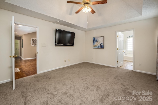 unfurnished bedroom with carpet, a raised ceiling, a ceiling fan, connected bathroom, and baseboards