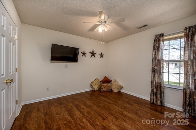 interior space featuring a textured ceiling, wood finished floors, a ceiling fan, visible vents, and baseboards