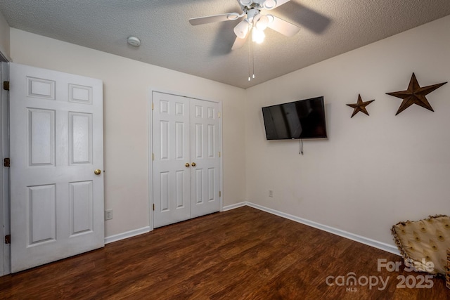 unfurnished bedroom featuring a closet, dark wood-type flooring, a ceiling fan, a textured ceiling, and baseboards