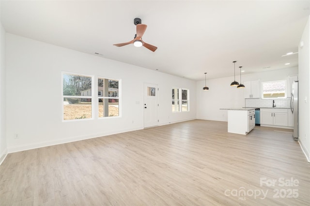 unfurnished living room featuring light wood finished floors, a wealth of natural light, and baseboards