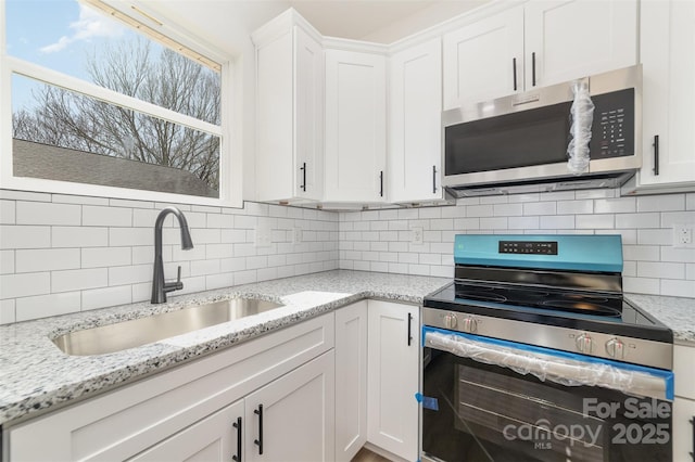 kitchen with tasteful backsplash, light stone countertops, stainless steel appliances, white cabinetry, and a sink