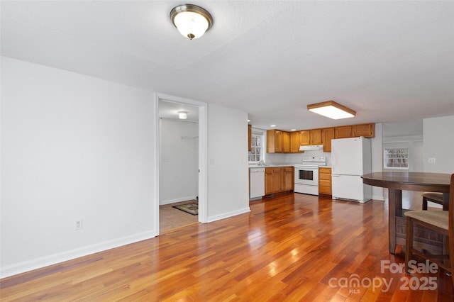 kitchen featuring brown cabinets, wood finished floors, white appliances, light countertops, and baseboards