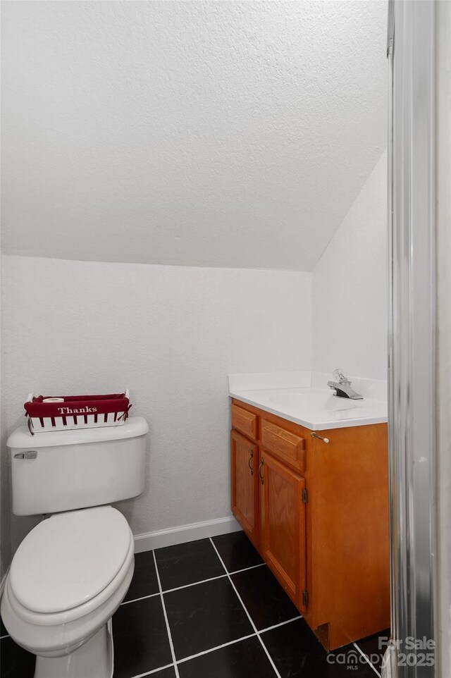 half bath featuring toilet, lofted ceiling, tile patterned flooring, baseboards, and vanity