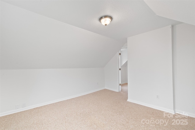 additional living space with vaulted ceiling, baseboards, and light carpet