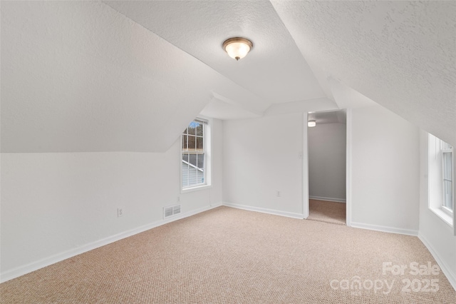 bonus room featuring visible vents, lofted ceiling, a textured ceiling, baseboards, and light colored carpet