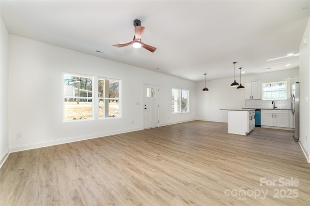 unfurnished living room with visible vents, light wood-style flooring, a sink, ceiling fan, and baseboards