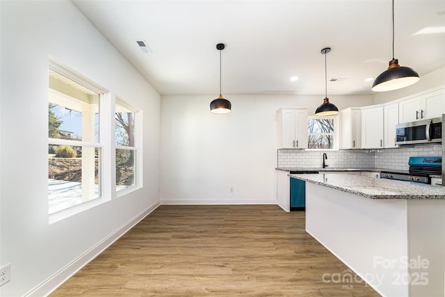 kitchen featuring white cabinets, decorative backsplash, light stone counters, stainless steel appliances, and light wood-style floors