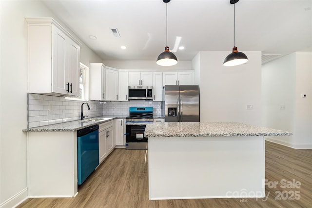 kitchen with stainless steel appliances, tasteful backsplash, white cabinetry, a sink, and a kitchen island