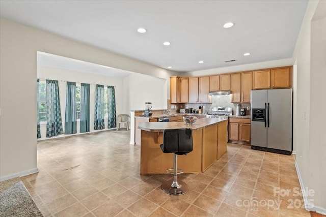 kitchen with a center island, under cabinet range hood, stainless steel refrigerator with ice dispenser, backsplash, and recessed lighting