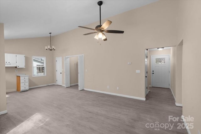 unfurnished living room featuring ceiling fan with notable chandelier, high vaulted ceiling, and baseboards