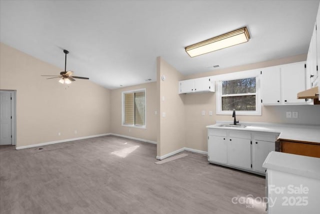 kitchen featuring lofted ceiling, light countertops, white cabinetry, a sink, and baseboards