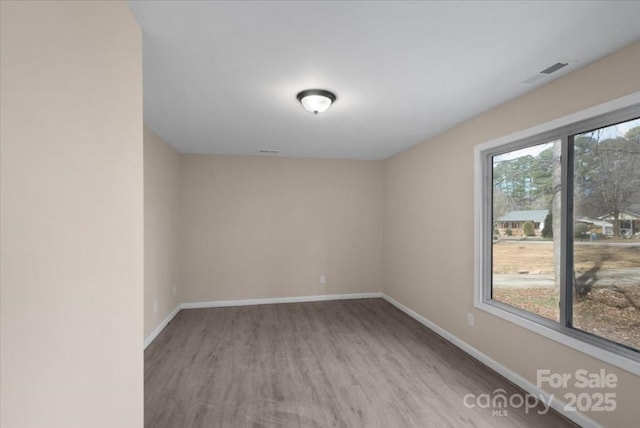 empty room featuring wood finished floors, visible vents, and baseboards