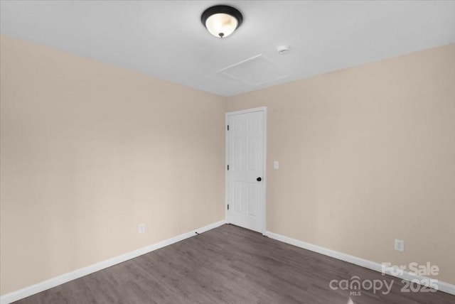 spare room with attic access, baseboards, and dark wood-style flooring