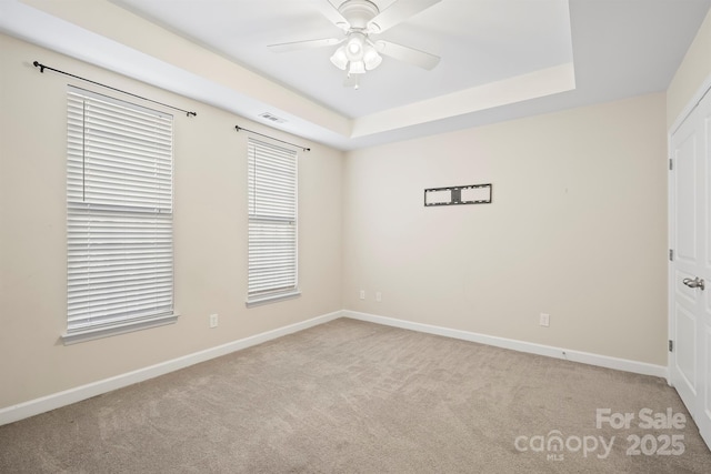 empty room featuring a ceiling fan, carpet, visible vents, and a tray ceiling