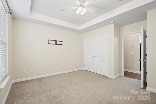 unfurnished bedroom featuring light carpet, a tray ceiling, a closet, and baseboards