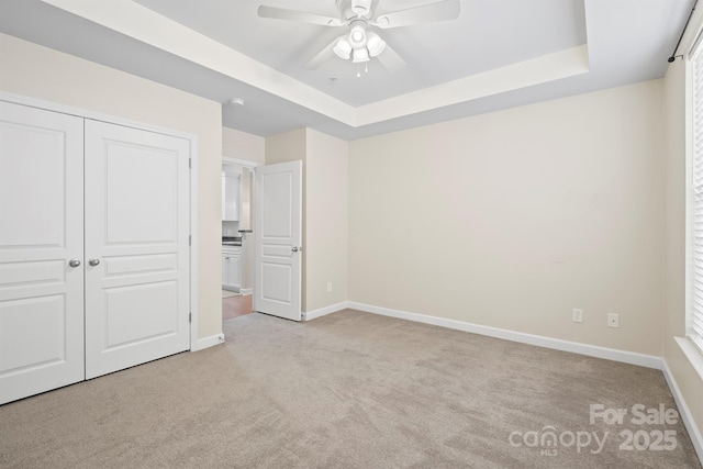 unfurnished bedroom with baseboards, carpet, a tray ceiling, and a closet