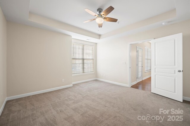 carpeted empty room with baseboards, a raised ceiling, and a ceiling fan