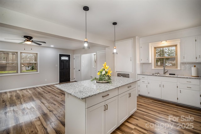 kitchen featuring decorative backsplash, white cabinets, wood finished floors, hanging light fixtures, and a sink