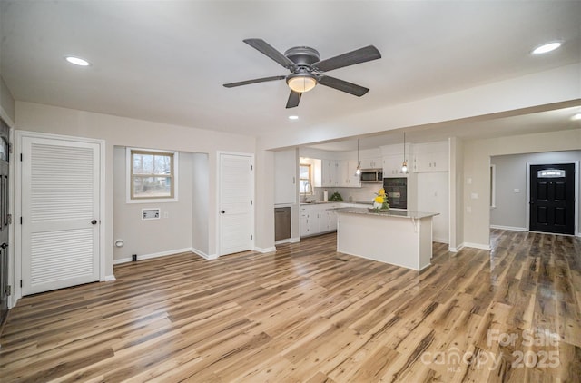 kitchen featuring a center island, light countertops, stainless steel microwave, light wood-style flooring, and white cabinets