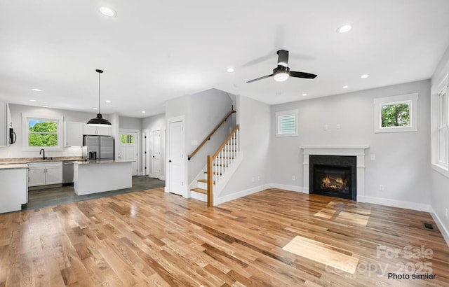 unfurnished living room with a wealth of natural light, recessed lighting, a sink, light wood-type flooring, and stairs