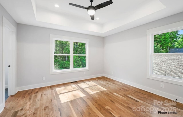 spare room featuring a tray ceiling, light wood-type flooring, and baseboards