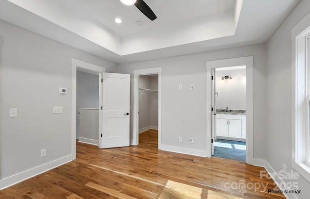 unfurnished bedroom featuring light wood-type flooring, a walk in closet, a tray ceiling, and baseboards