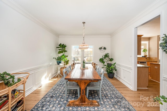 dining space featuring ornamental molding, light wood-style flooring, and a decorative wall