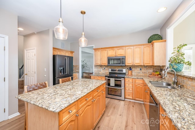 kitchen with appliances with stainless steel finishes, light wood-style floors, a sink, and a kitchen island