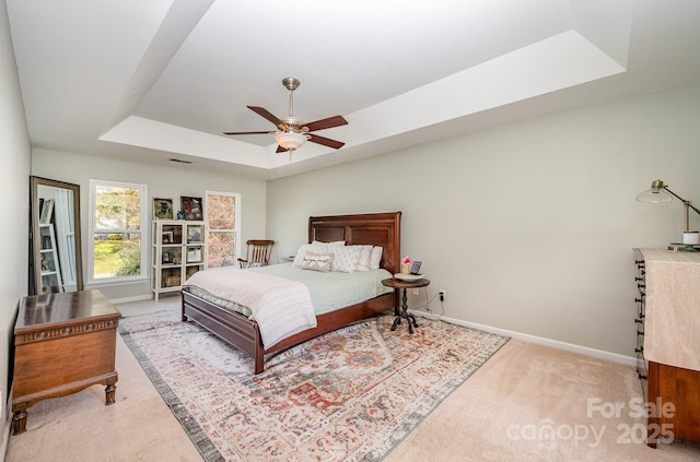 bedroom with ceiling fan, visible vents, baseboards, a tray ceiling, and carpet