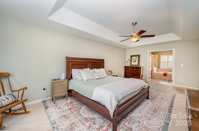 bedroom with a raised ceiling, ensuite bathroom, a ceiling fan, light carpet, and baseboards