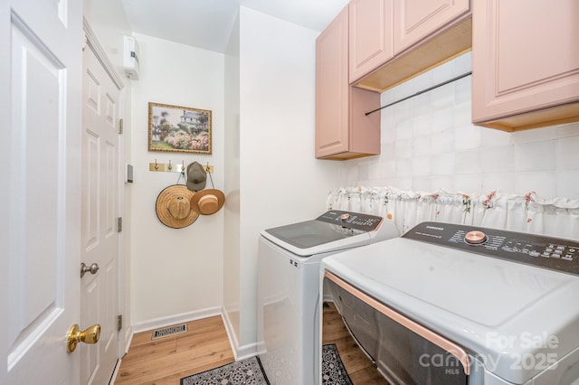 clothes washing area with cabinet space, visible vents, light wood-style flooring, washer and dryer, and baseboards