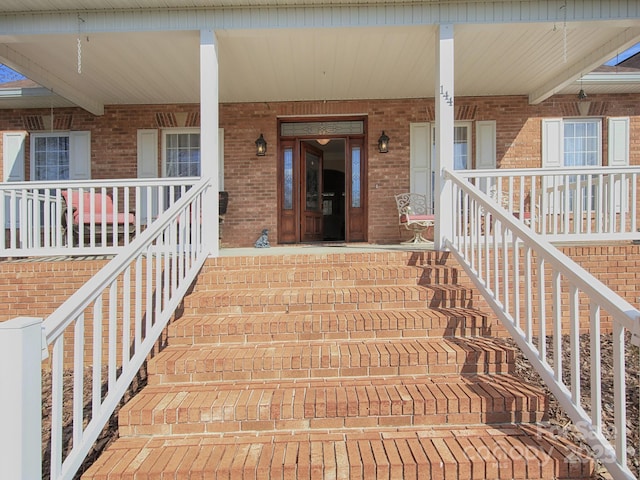 property entrance featuring a porch and brick siding