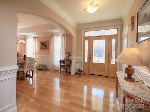 entryway featuring arched walkways, ornamental molding, light wood-style flooring, and a decorative wall