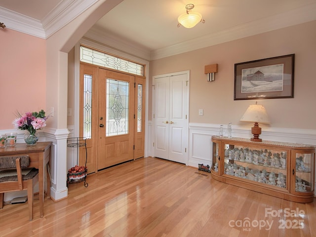 foyer featuring light wood-style floors, arched walkways, wainscoting, and crown molding