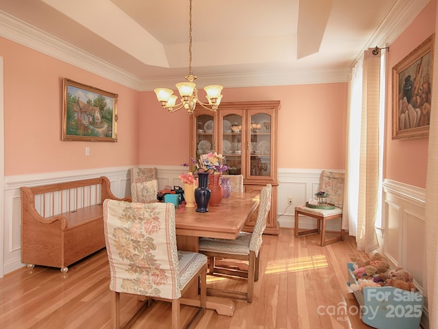 dining area with light wood finished floors, wainscoting, a raised ceiling, and an inviting chandelier