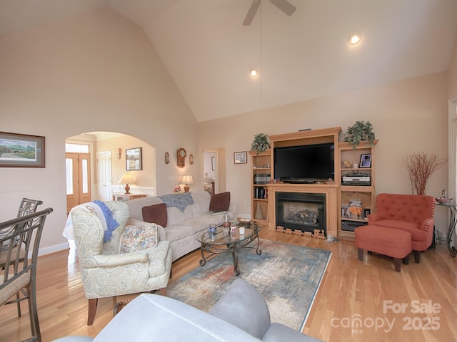 living room with arched walkways, high vaulted ceiling, light wood finished floors, and a glass covered fireplace