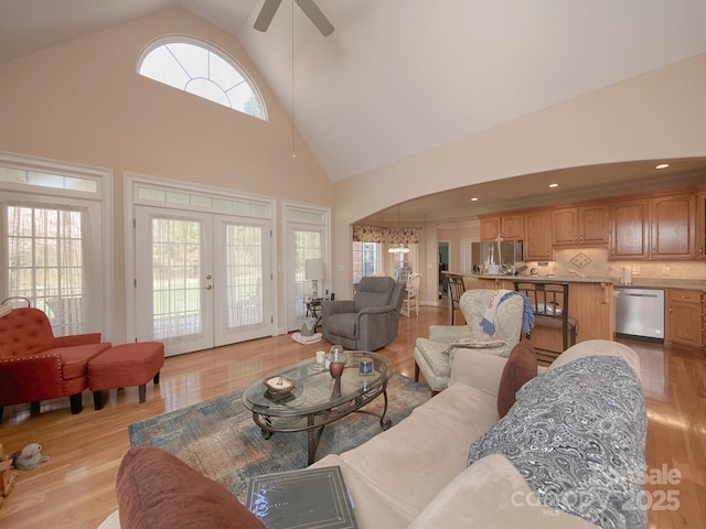 living area with light wood-style floors, high vaulted ceiling, arched walkways, and french doors