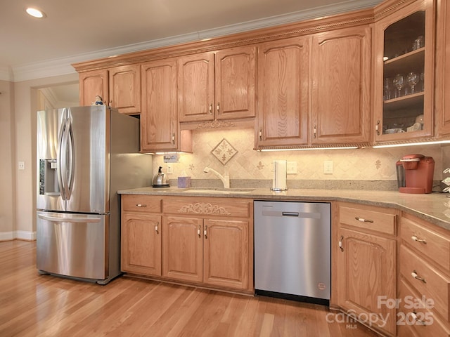 kitchen featuring stainless steel appliances, light wood-style floors, glass insert cabinets, ornamental molding, and a sink